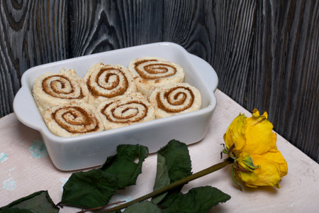Baking cinnabons. The cinnamon dough is in the baking dish. Background from black pine boards. Nearby is a dried rose.の写真素材