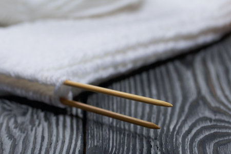 Knitting with needles. Wooden knitting needles and white threads. On black pine boards.の写真素材