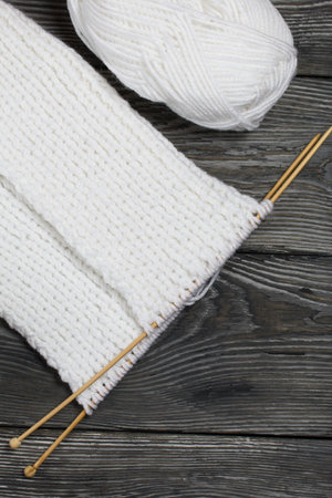 Knitting with needles. Wooden knitting needles and white threads. On black pine boards.