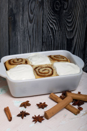 Baking cinnabons. The cinnamon rolls is in the baking dish. Next to it are cinnamon sticks and anise...