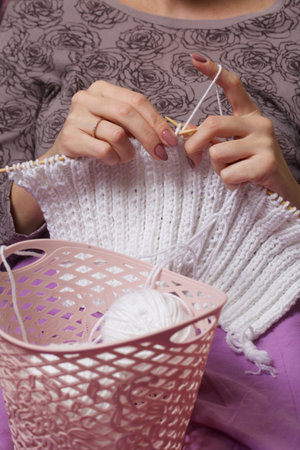 The woman knits. Sitting in my pajamas under the covers. Nearby is a basket with skeins of thread. Close-up shot.の写真素材