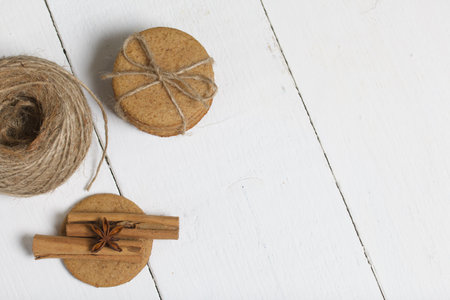 Gingerbread cookies tied with twine. Nearby are cinnamon sticks, anise and a skein of twine. On...