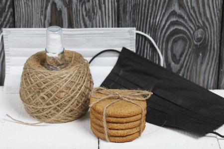 Gingerbread cookies tied with twine. Nearby are medical masks and antiseptic. On boards painted white.の写真素材