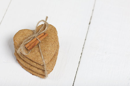 Heart-shaped gingerbread cookie tied with twine. It has a cinnamon stick on it. On boards painted white. Close-up shot.の写真素材