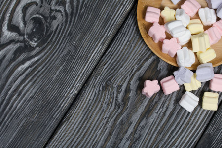 Marshmallows on a wooden plate. A little scattered nearby. On black pine planks.の写真素材