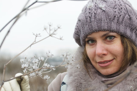 A woman in winter clothes walks in the park. Around the dried plants covered with ice crust and...