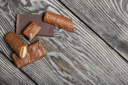Chopped up chocolate bar. Filled with caramel and nuts. Nearby are pieces of chocolate. On black pine boards.の写真素材