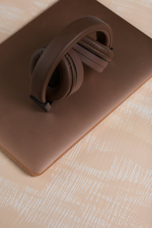 Fragment of a pink notebook. Nearby are wireless headphones in brown. The surface is painted in white and beige.の写真素材