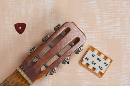 Acoustic guitar neck, tuning fork and pick. Against a background painted in white and beige.