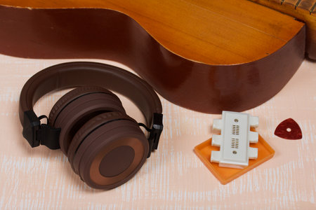 Fragment of acoustic guitar, tuning fork and pick. Nearby are wireless headphones. Against a...