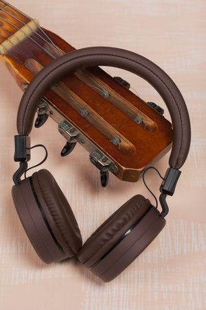 Fragment of acoustic guitar and wireless headphones. Against a background painted in white and...