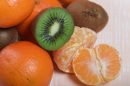 Orange tangerines. One without a peel. Kiwi fruit cut in half. Juicy green flesh is visible. Close-up shot.の写真素材