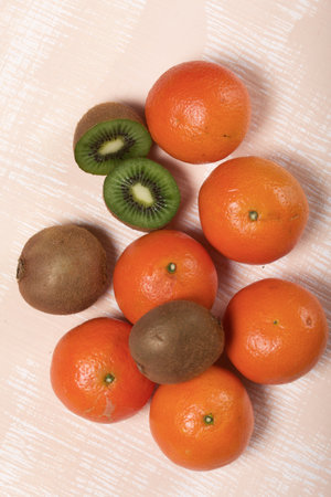 Several orange tangerines. Kiwi fruit cut in half. Juicy green flesh is visible. Lie on a beige surface.の写真素材