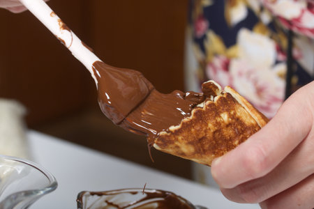 A woman covers waffle cones with chocolate. Dessert preparation.の写真素材