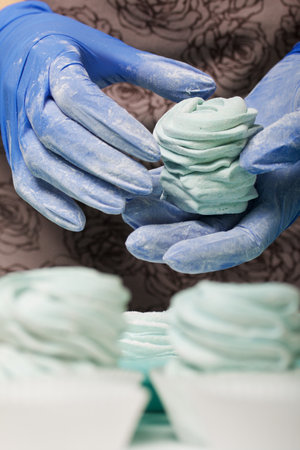 Woman in rubber gloves makes marshmallows. Sprinkles it with powdered sugar. Dessert lies on the table surface.の写真素材