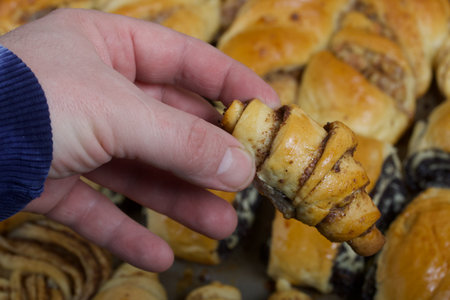 Male hand with a bun. Rich pastries. The buns are on a baking sheet. Filling with poppy seeds,...