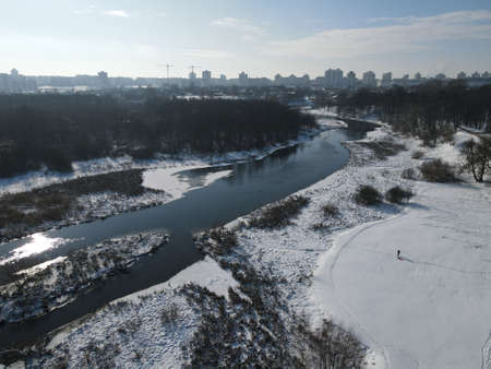 Urban winter landscape from above. Multi-storey buildings and trees in the city park are visible. River flows.の写真素材