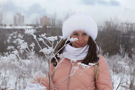 Portrait of a girl for a walk in a winter park. The plants are covered with frost and snow.