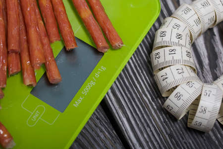 Sausage on scales and measuring tape. On pine boards. A day without diets.の写真素材