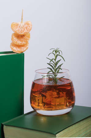 Alcoholic cocktail. Garnished with rosemary slices and tangerine wedges. Nearby are books. Close-up shot.の写真素材