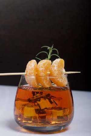 Alcoholic cocktail. Garnished with rosemary slices and tangerine wedges. Close-up shot.