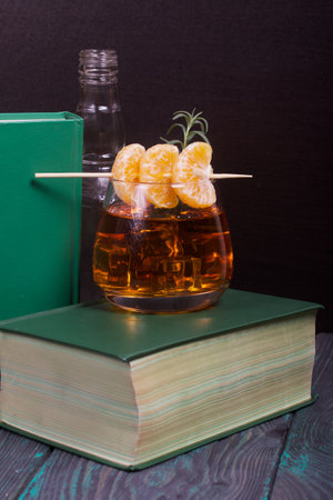 Alcoholic cocktail. Garnished with rosemary slices and tangerine wedges. Nearby are books. Close-up shot.の写真素材