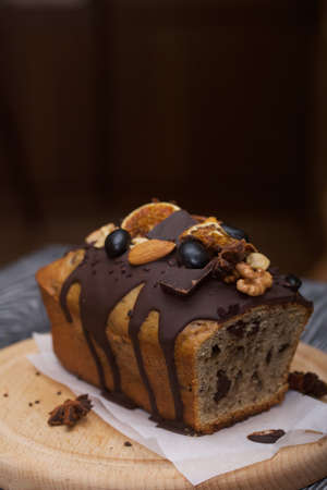 Banana bread garnished with nuts and dried fruits. A slice of bread is visible. Close-up shot.