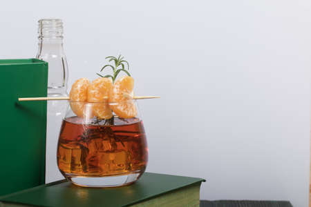 Alcoholic cocktail. Garnished with rosemary slices and tangerine wedges. Nearby are books. Close-up...