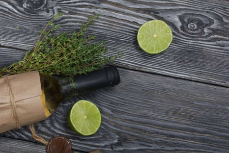 Alcohol bottle. Wrapped in paper. Nearby thyme and lime halves. On pine boards.の写真素材
