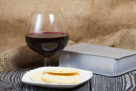 A glass of dry red wine and broken unleavened bread lie on a plate. To celebrate the Lord's Supper. Nearby lies the Bible.の写真素材