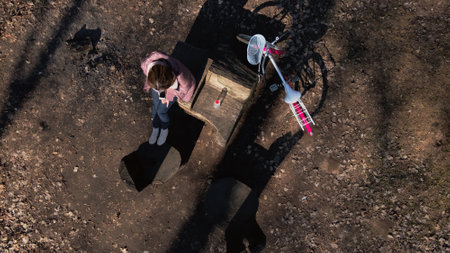 Girl on a bike ride walk in the spring park. Sits on a bench and looks at the phone. Her bike is...