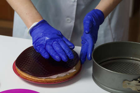 A woman prepares a marshmallow cake. Places a layer of jelly and marshmallows on the biscuit. Works with a mask and gloves.の写真素材