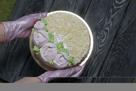 A woman prepares a marshmallow cake. The cake is decorated with marshmallow roses and almond petals....