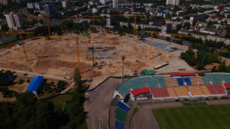 Football stadium in the city park. A new arena is being built nearby. A green field and stands are visible, painted in different colors. Aerial photography.のeditorial素材