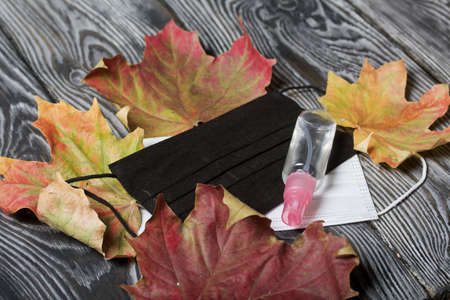 Medical masks and antiseptic. Nearby is an autumn maple leaf. On brushed pine boards.
