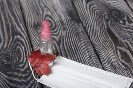 Medical mask and antiseptic. Nearby is an autumn maple leaf. On brushed pine boards.の写真素材