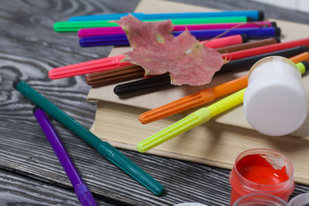 School accessories. Felt-tip pens and gouache of different colors lie on pine boards. Nearby is a...