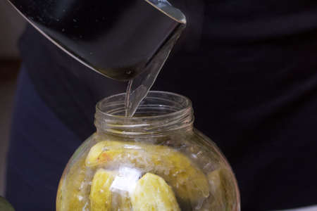 A woman pours boiling marinade over cucumbers in jars. Pickling cucumbers at home. Vegetable harvest...