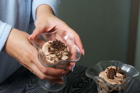 A woman places a dessert of cream and biscuit crumbs on the table. Close-up shot.の写真素材