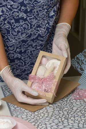 A woman decorates a package of homemade marshmallows with ribbon and lagurus. Demonstrates to the camera. Nearby are bouquets of zephyr roses and tulips.の写真素材