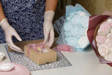 A woman is packing marshmallows in craft packaging. Ties a ribbon on a bow. Nearby are bouquets of marshmallow roses and tulips.の写真素材