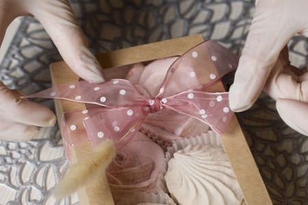A woman decorates a package of homemade marshmallows with ribbon and lagurus. Nearby are bouquets of marshmallow roses and tulips. Close-up shot.の写真素材