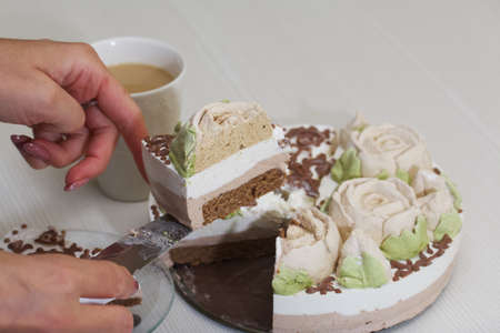 A woman cuts a bird's milk cake, decorated with marshmallow roses and chocolate. Nearby is a cup of...