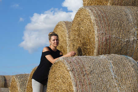 Girl posing near a stack of straw. Straw rolls, stacked in a pyramid. Close-up shot.