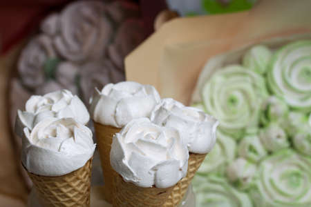 Homemade marshmallows are spread out on the table surface. Zephyr in a waffle cone. Made in the shape of a rose. Close-up shot.の写真素材