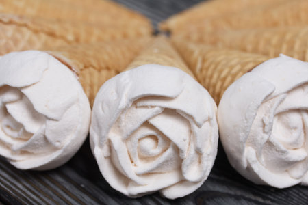 Homemade marshmallows are spread out on the table surface. Zephyr in a waffle cone. Made in the shape of a rose. Close-up shot.の写真素材