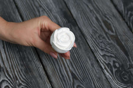 A woman holds a homemade marshmallow in her hands. Marshmallow in a waffle cone. Made in the shape of a rose. Close-up shot. Against the background of pine boards.の写真素材