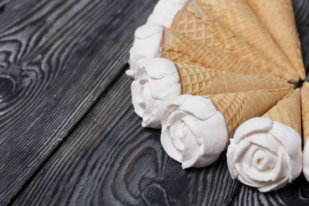 Homemade marshmallows are spread out on the table surface. Zephyr in a waffle cone. Made in the shape of a rose. Close-up shot.の写真素材