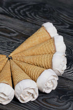 Homemade marshmallows are spread out on the table surface. Zephyr in a waffle cone. Made in the shape of a rose. Close-up shot.の写真素材