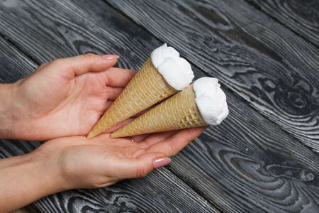 A woman holds a homemade marshmallow in her hands. Marshmallow in a waffle cone. Made in the shape of a rose. Close-up shot. Against the background of pine boards.の写真素材